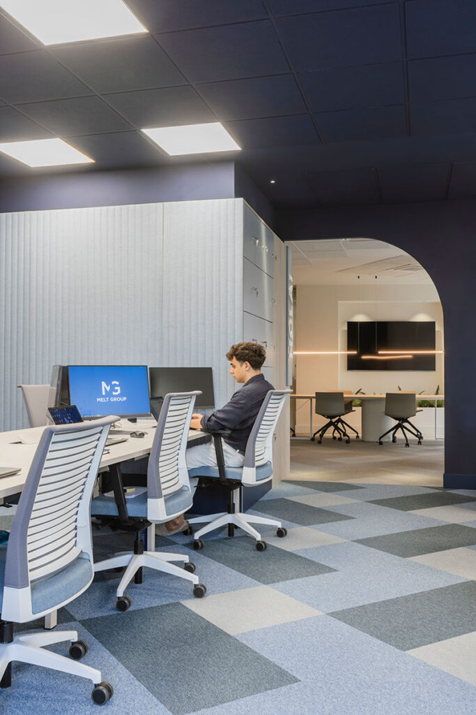 Puestos de trabajo con sillas ergonómicas blancas y moqueta ajedrezada azul en las oficinas de Melt Group