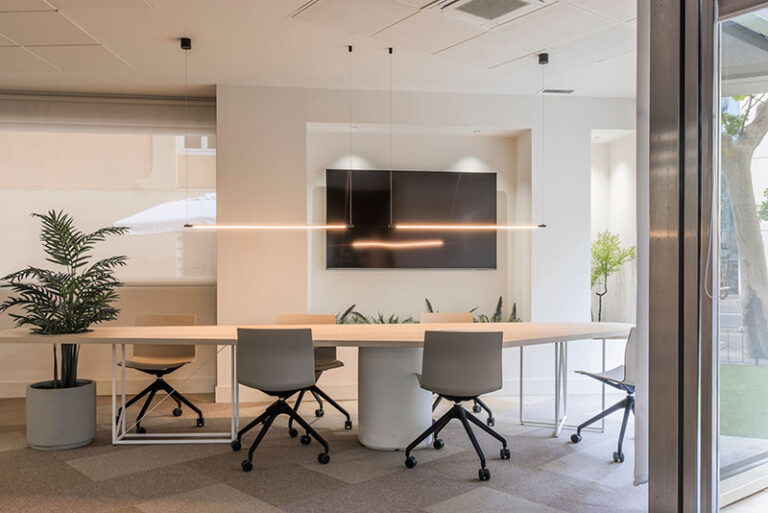 Zona de trabajo abierta y luminosa con mesas blancas y arcos azules en las oficinas de Melt Group en Valencia