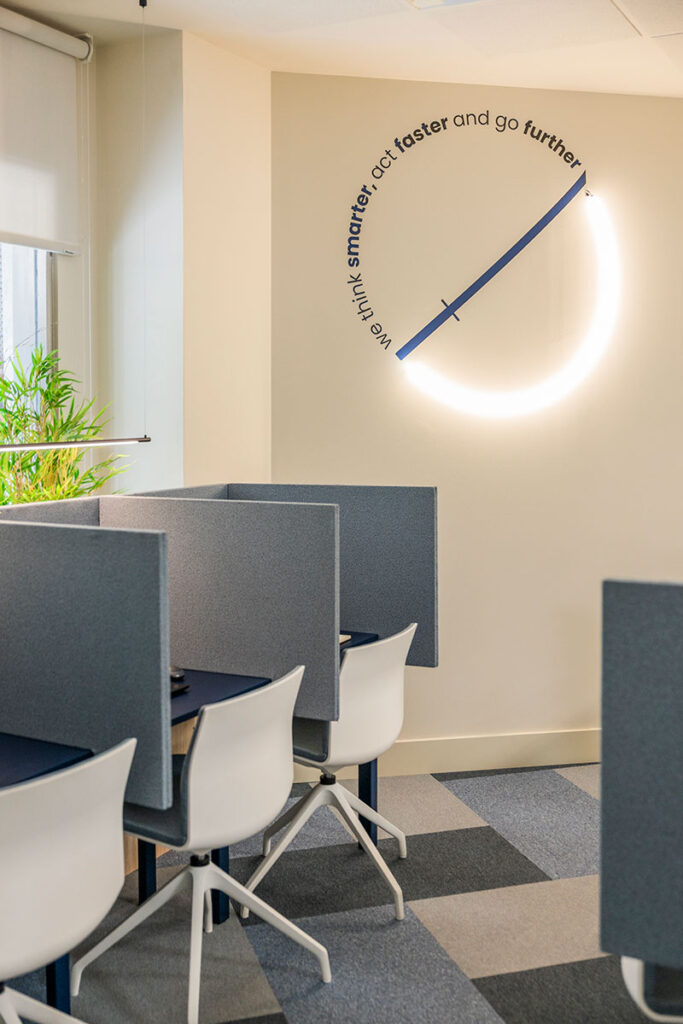 Puestos de trabajo con paneles separadores y aro de luz con frase inspiradora en las oficinas de Melt Group