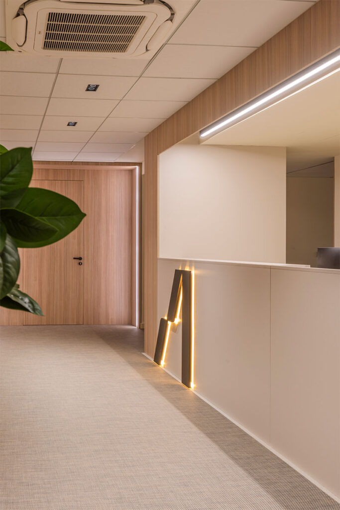 Mostrador de recepción blanco con la letra A retroiluminada y revestimiento de madera en las oficinas de Arisnova