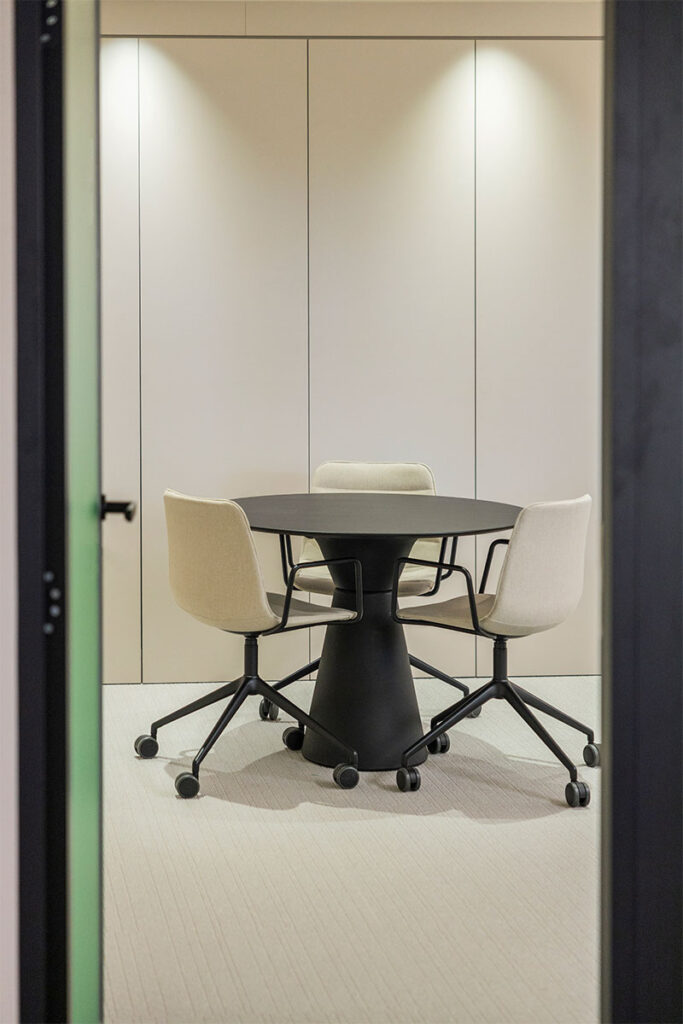 Sala de reuniones pequeña con mesa redonda negra y sillas tapizadas en beige en las oficinas de Arisnova