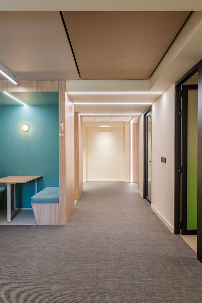 Pasillo con cabina de trabajo turquesa, techo acústico y líneas de luz LED en las oficinas de Arisnova